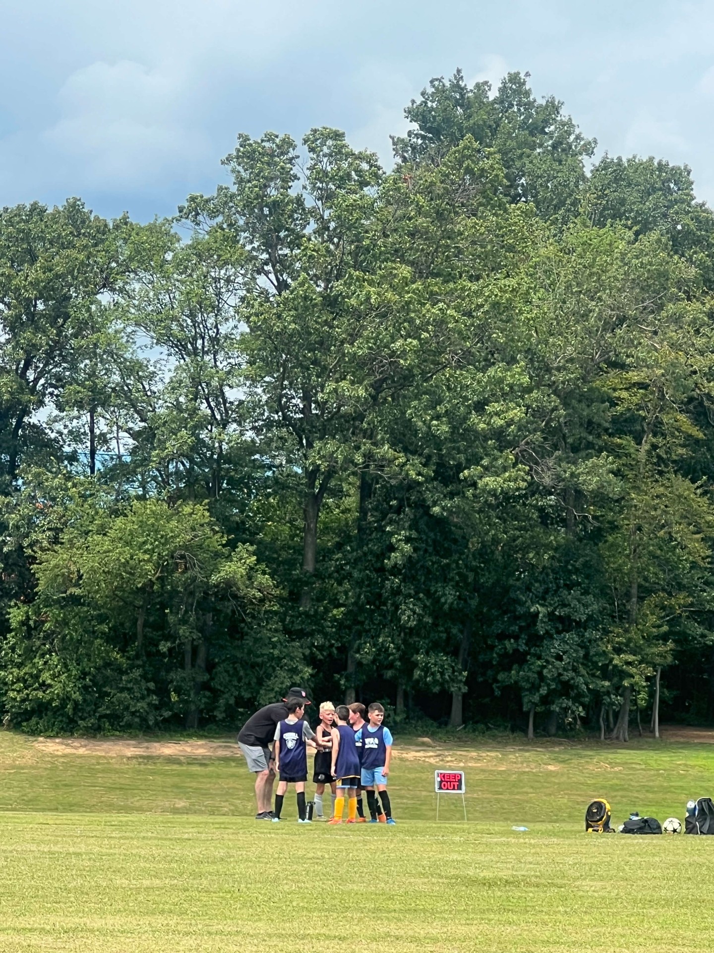 2025 — Coach huddling with a youth team in front of the trees
