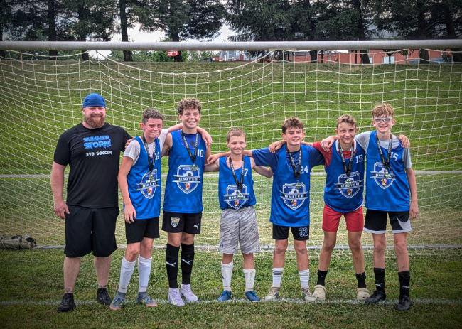 Blue team and coach posing with medals in front of a goal