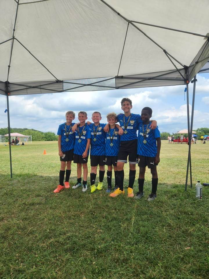 Blue team posing with medals under a tent on the grass